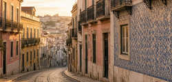 Illustrative image: a cobbled Lisbon street with tram tracks and tiled facades in late-afternoon light